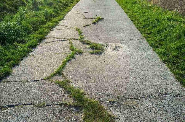 Cracked and damaged concrete driveway with visible wear and weeds growing through the surface in Beachwood, OH